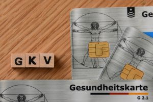 Drei Gesundheitskarten der deutschen Krankenasse auf einer hölzernen Oberfläche liegend. Der Schriftzug "GKV" befindet sich links daneben.