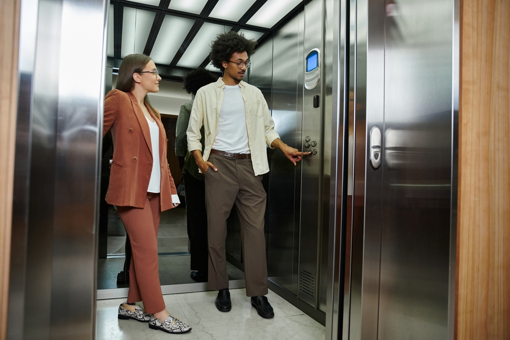 Zwei Menschen in einem Treppenlift. Der Mann betätigt den Button, um den Treppenlift zu verwenden.